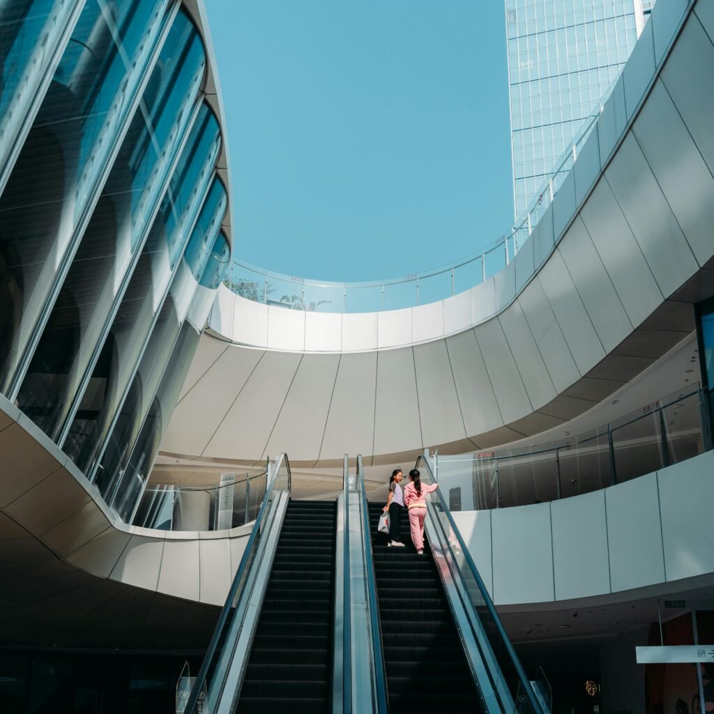 Two adults on an escalator within a sleek modern architectural structure under a clear blue sky.